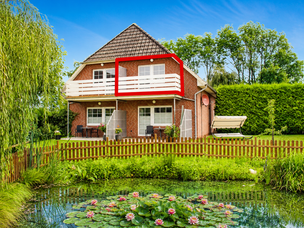 Ein rotes Backsteinhaus mit weißem Balkon im Obergeschoss, umgeben von einem Garten und einem Teich