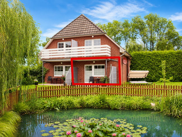Haus mit rotem Balkon in einem üppigen Garten neben einem Teich