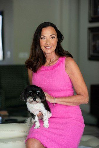 A woman in a pink dress is holding a small black and white dog.