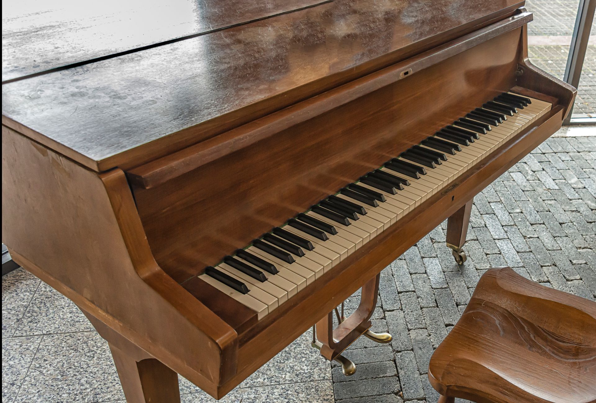 Wooden upright piano with open lid and a matching stool.
