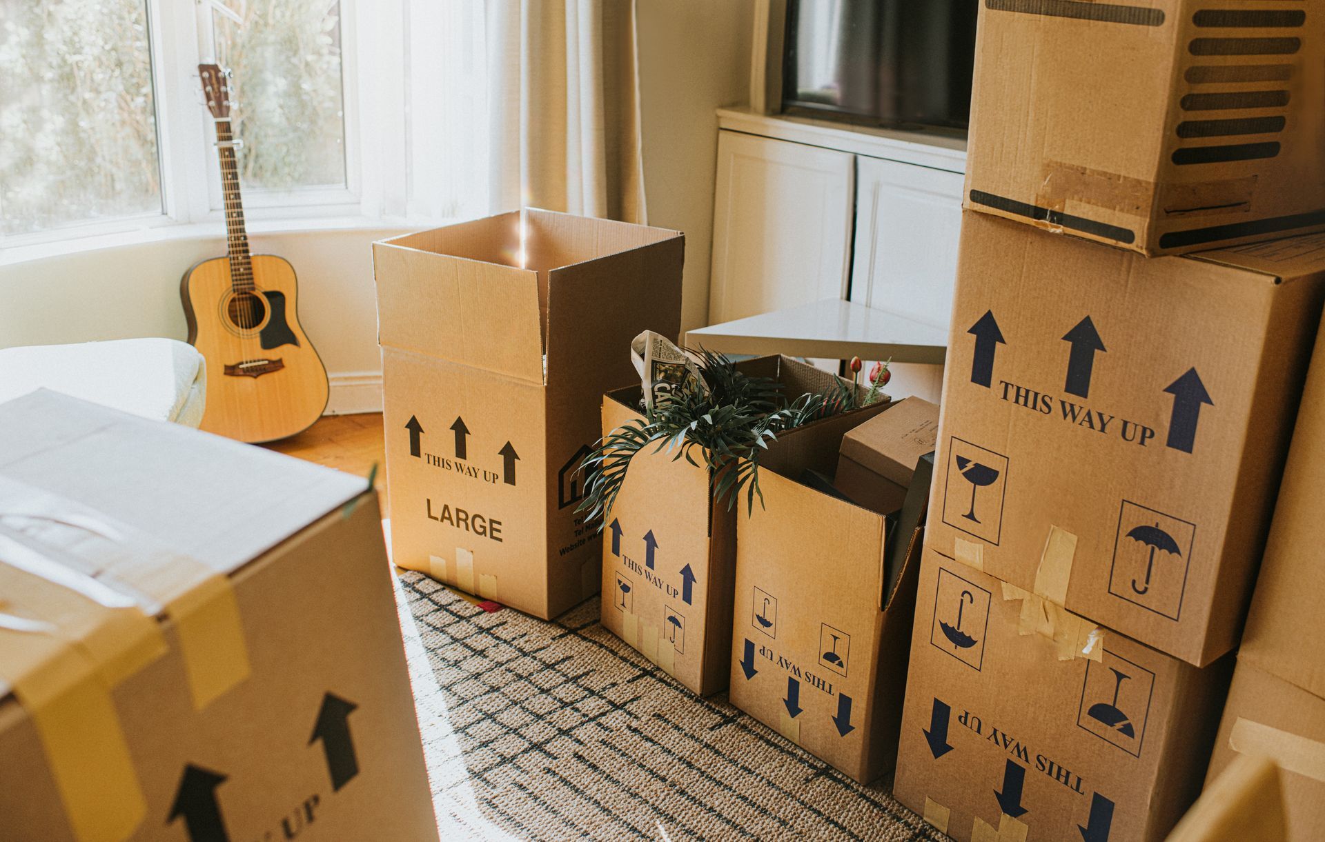 Boxes stacked in a room, ready for moving. An acoustic guitar rests by a window.