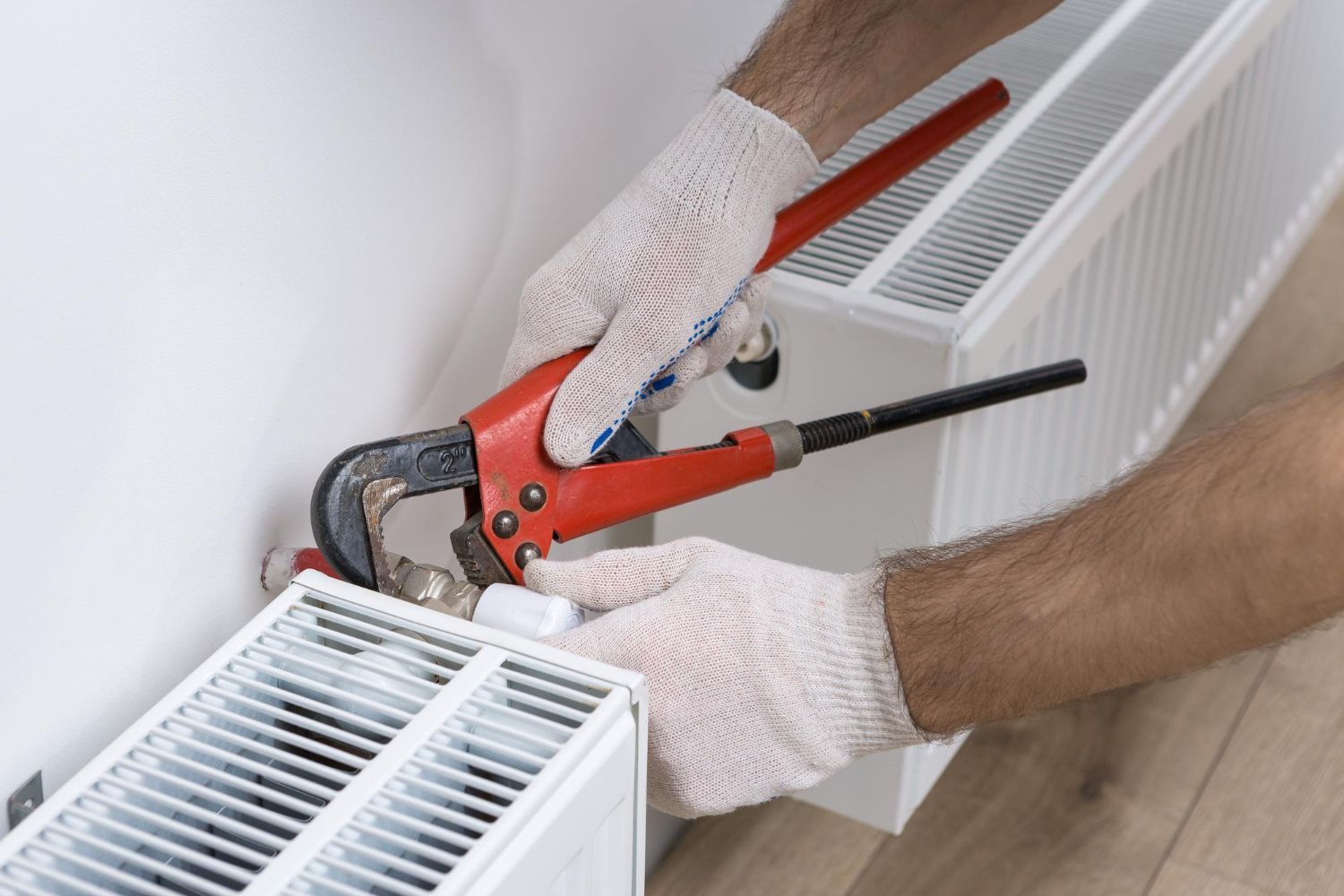 Gloved hands using a red pipe crimping tool on a white radiator pipe connection