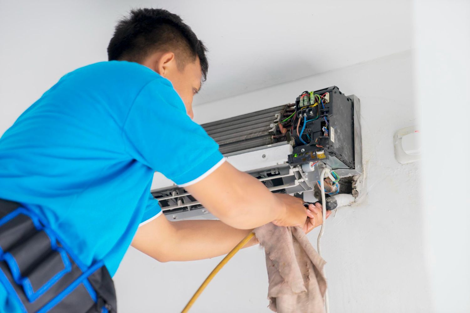 Technician cleaning a wall-mounted air conditioner with a cloth and hose