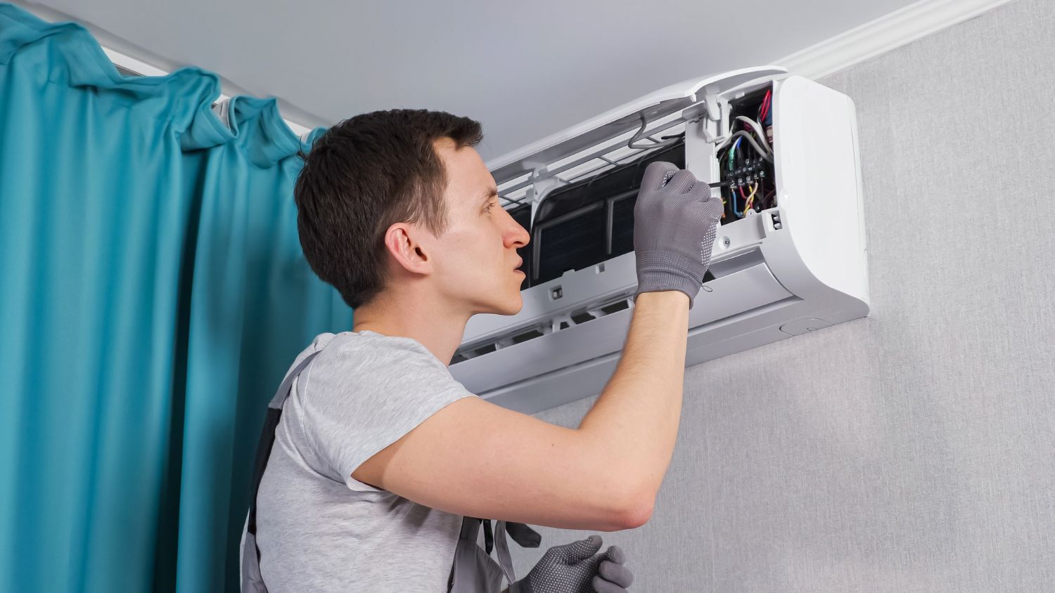 Technician repairing a wall-mounted air conditioner indoors, with tools and exposed wiring