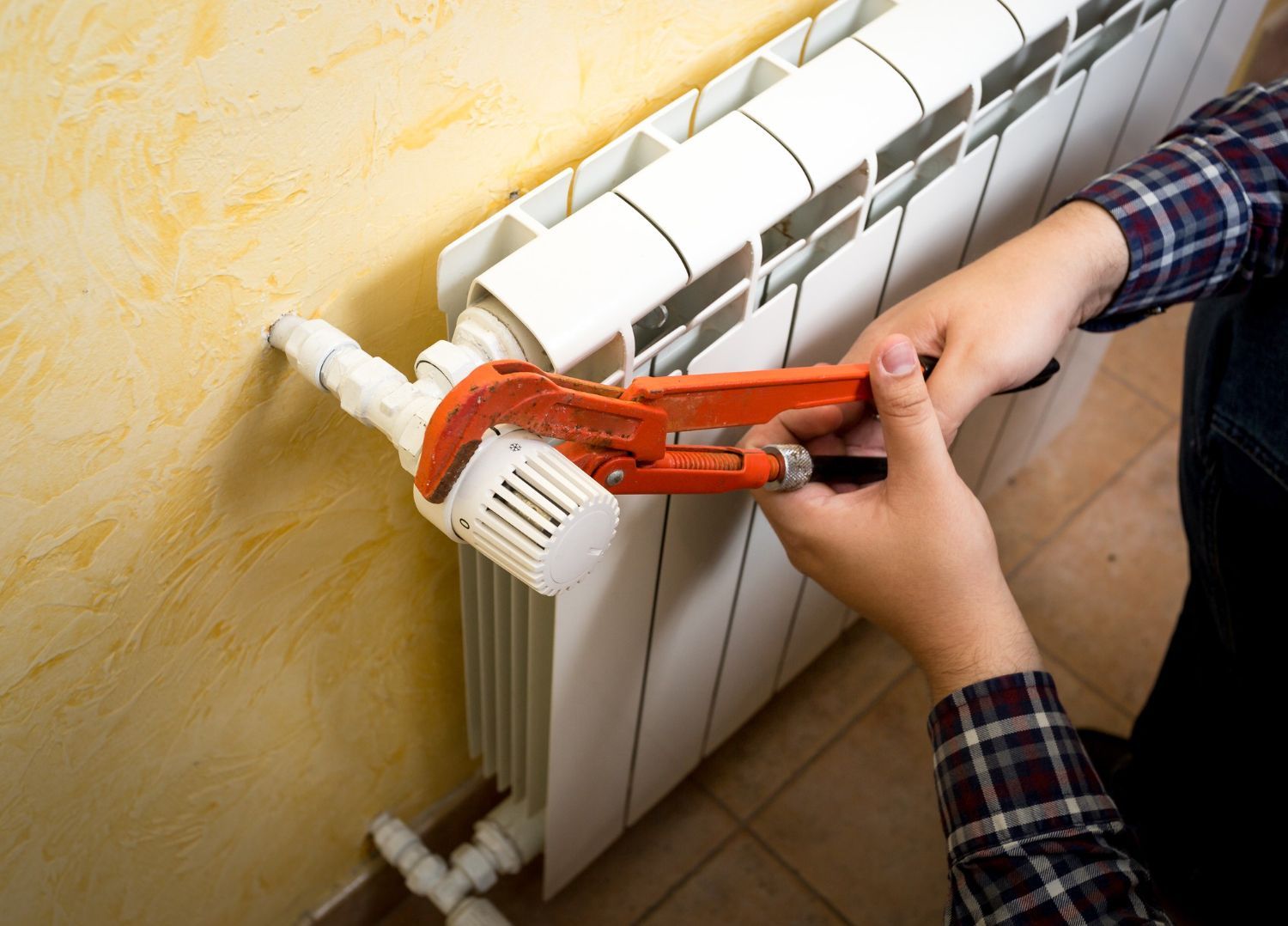 Hands using an orange wrench to adjust a white radiator near a yellow wall