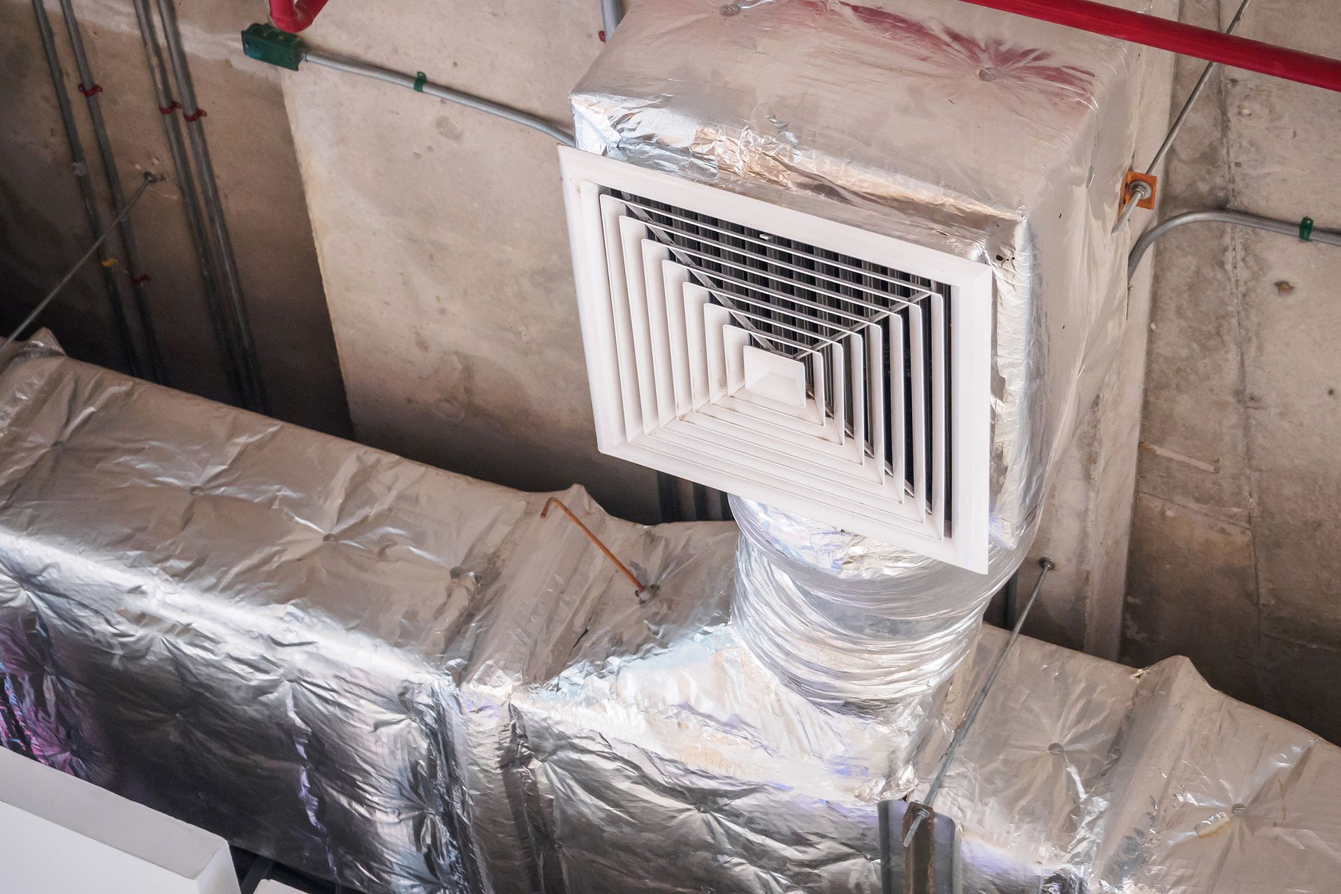 Foil-wrapped HVAC ductwork and a ceiling vent in an industrial room