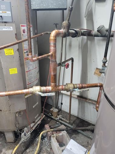 Copper pipes and a water heater in a cramped utility room with debris on the floor