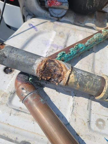 Corroded metal pipes and fittings with heavy rust damage on a work surface.