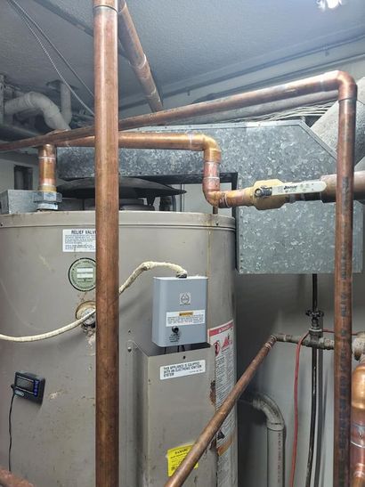 Basement water heater with copper pipes, gas control box, and ductwork in a utility room.