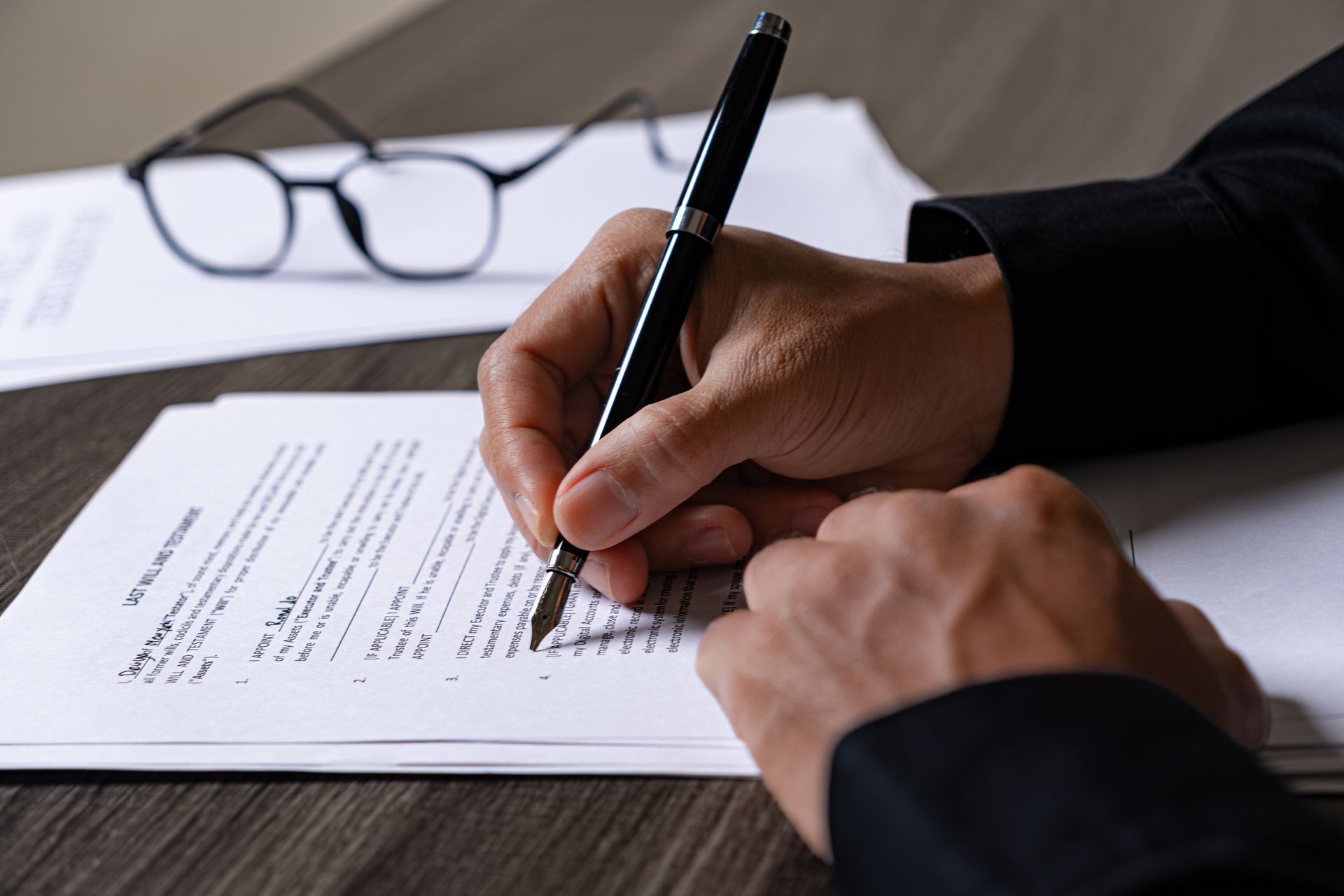 Close-up of hands signing a legal will document with a pen.
