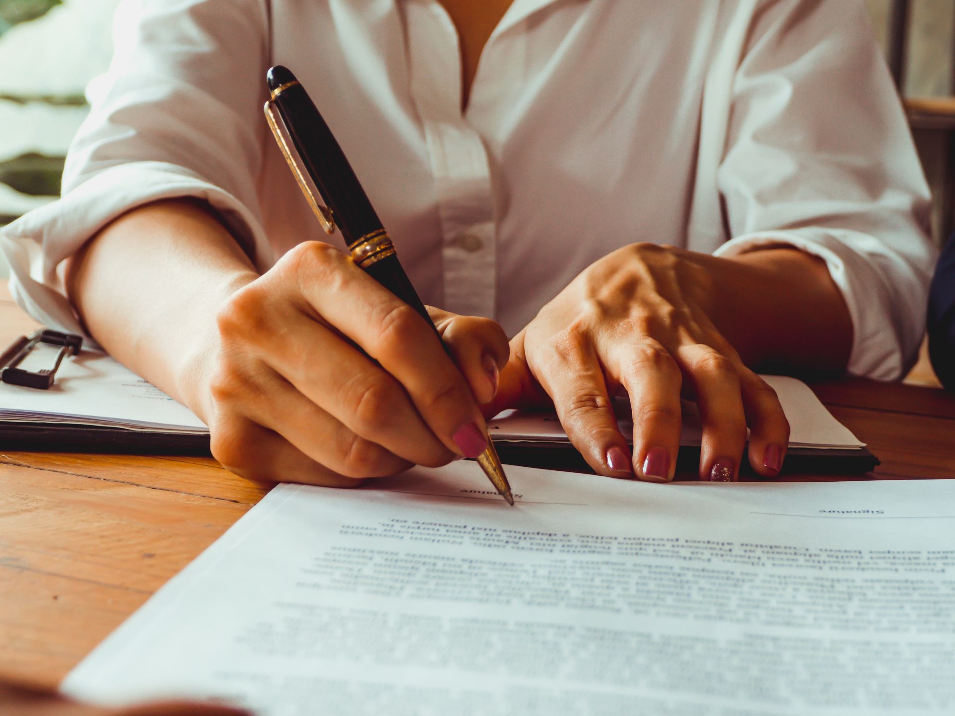 Person signing a document with a pen on a desk during a legal or business agreement. Person signing a document with a pen on a desk during a legal or business agreement.