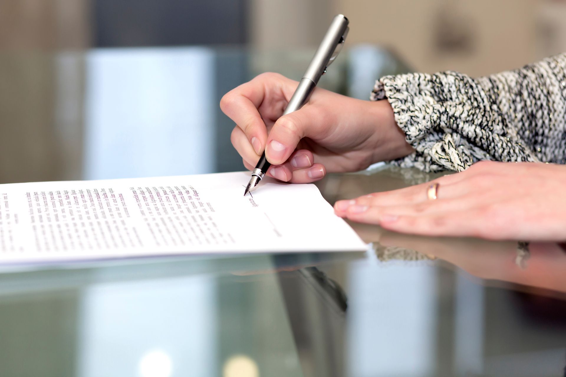 Person signing a printed document with a pen on a glass-top desk.