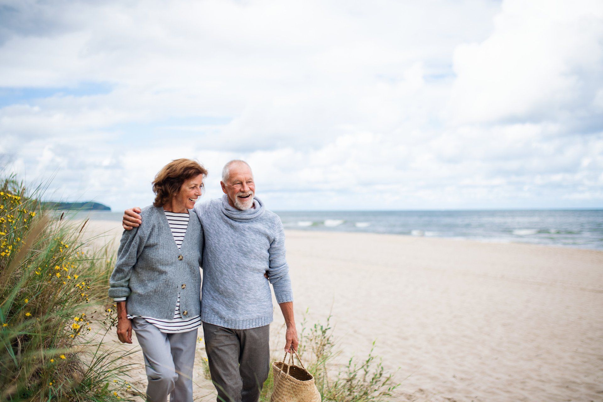 Elderly couple walking on a beach, arm-in-arm, enjoying the seaside.