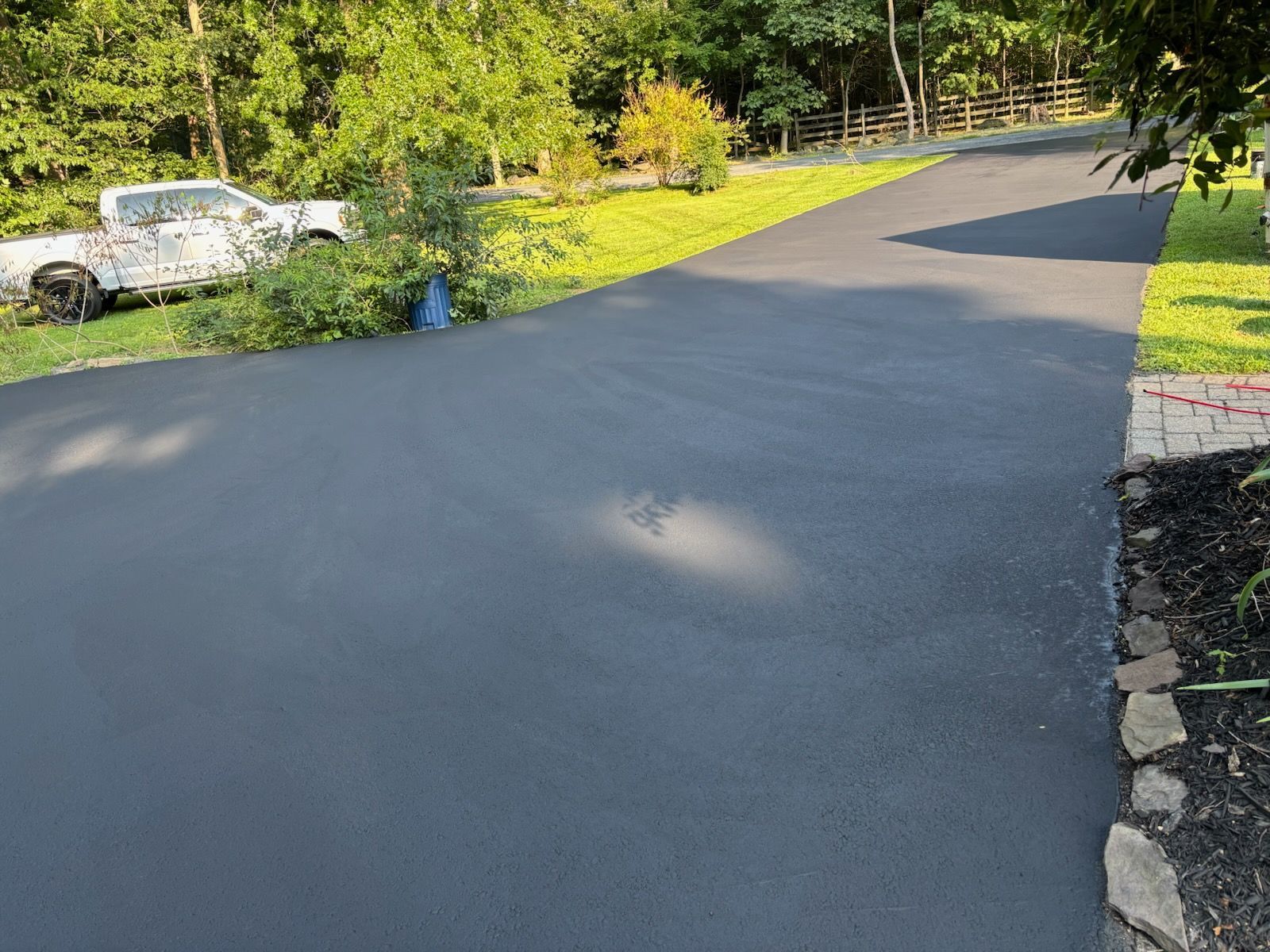 Newly paved black asphalt driveway with a truck and green grass on the sides.