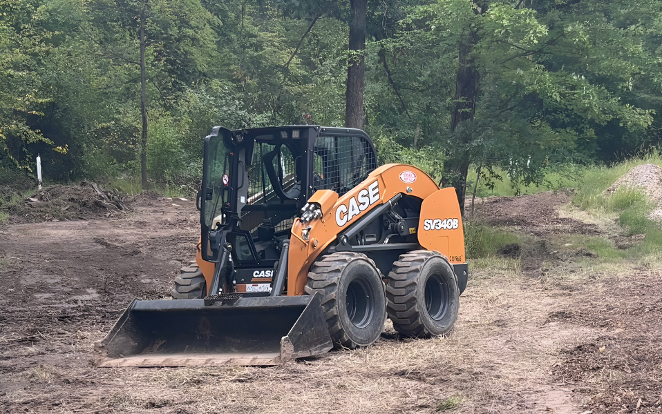 Orange Case skid steer loader on a dirt path, working in a wooded area.