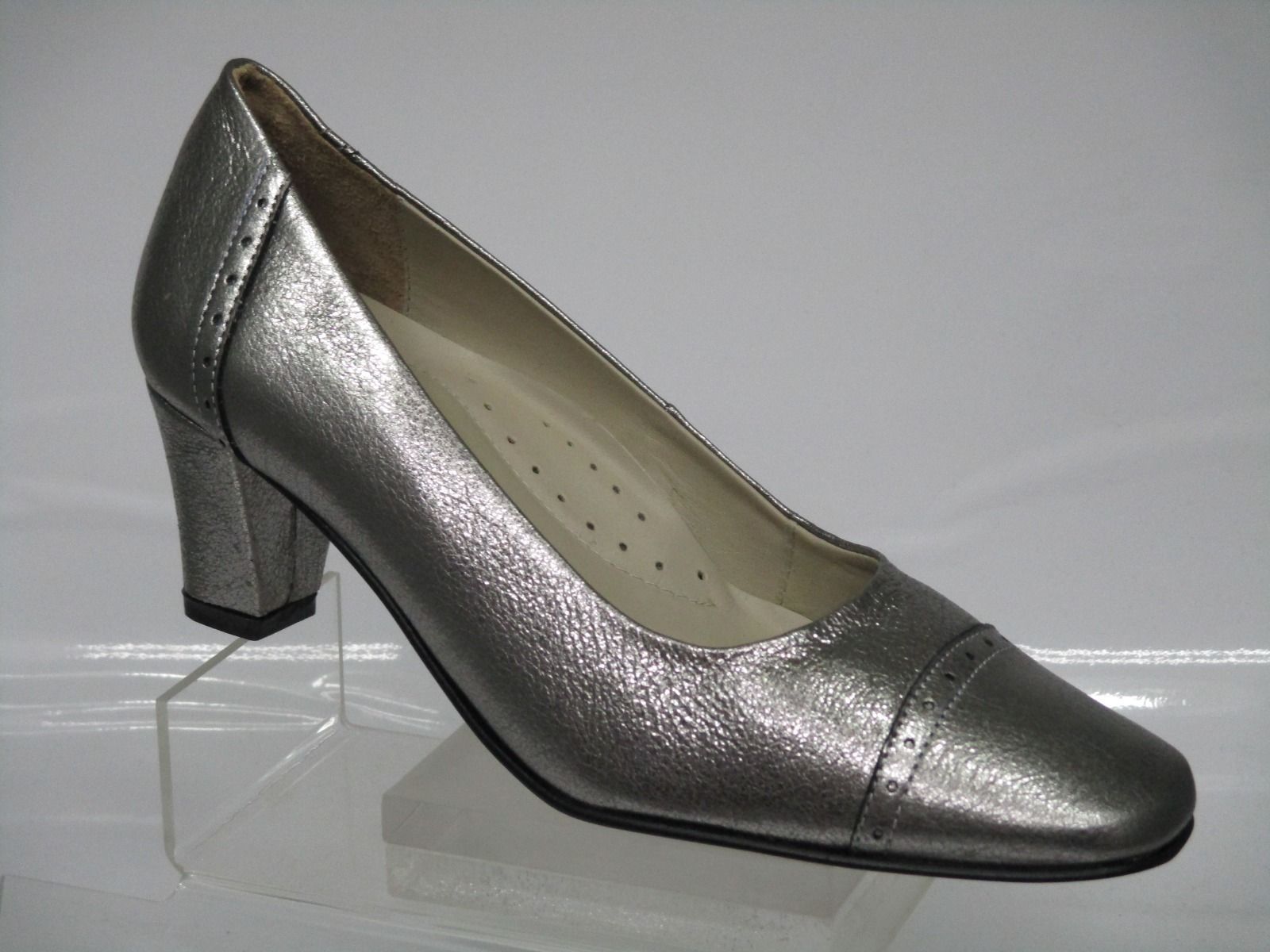 Zapatos de tacón plateados metalizados para mujer sobre un expositor transparente.