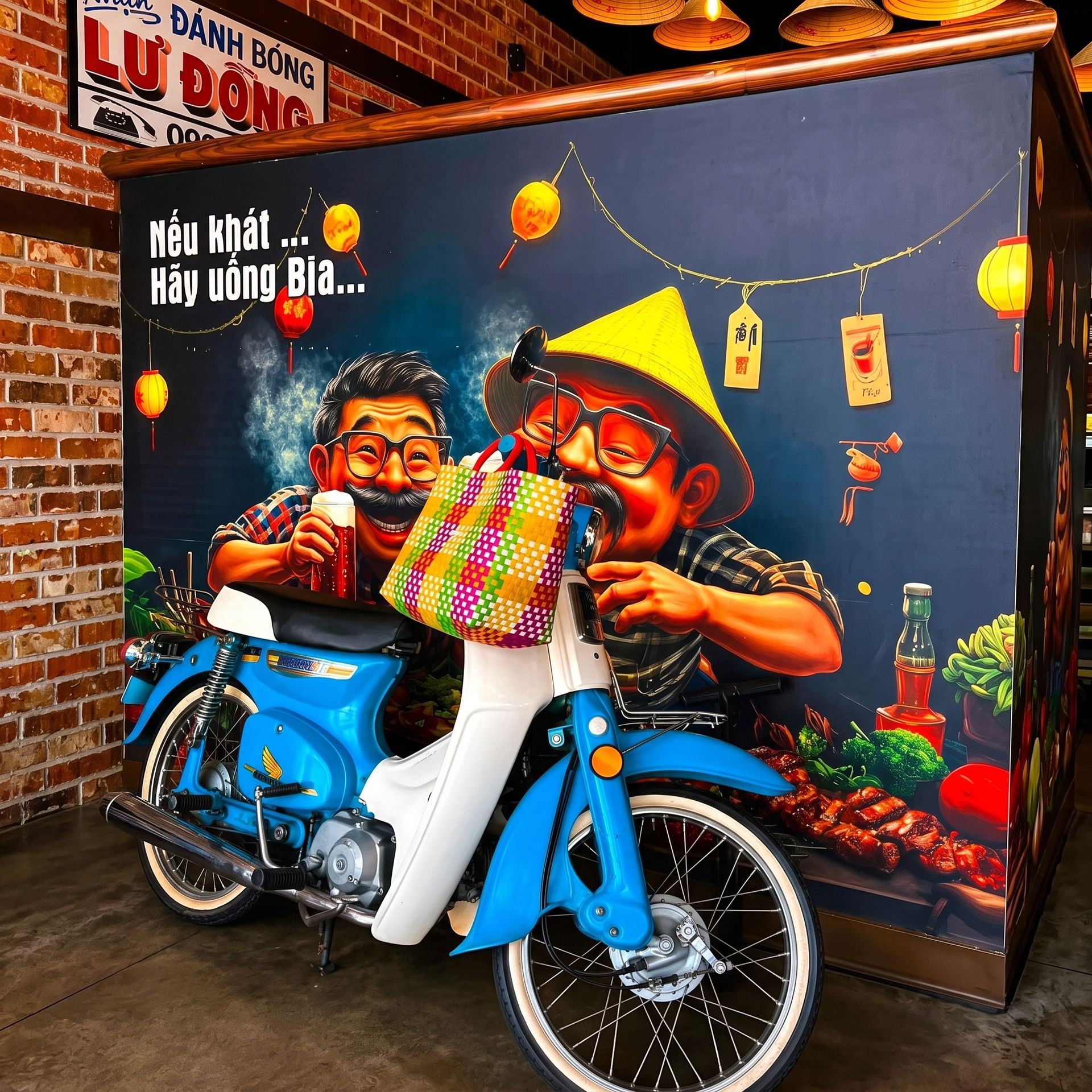 Blue motorbike display in front of a colorful Vietnamese beer-themed mural and sign.