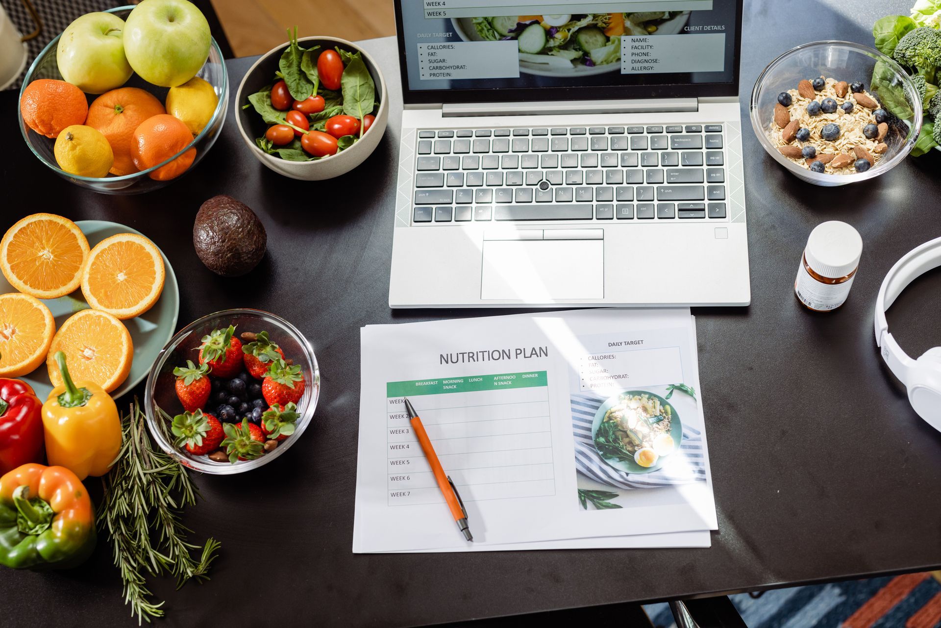 A laptop computer is sitting on a table next to bowls of fruit and vegetables.