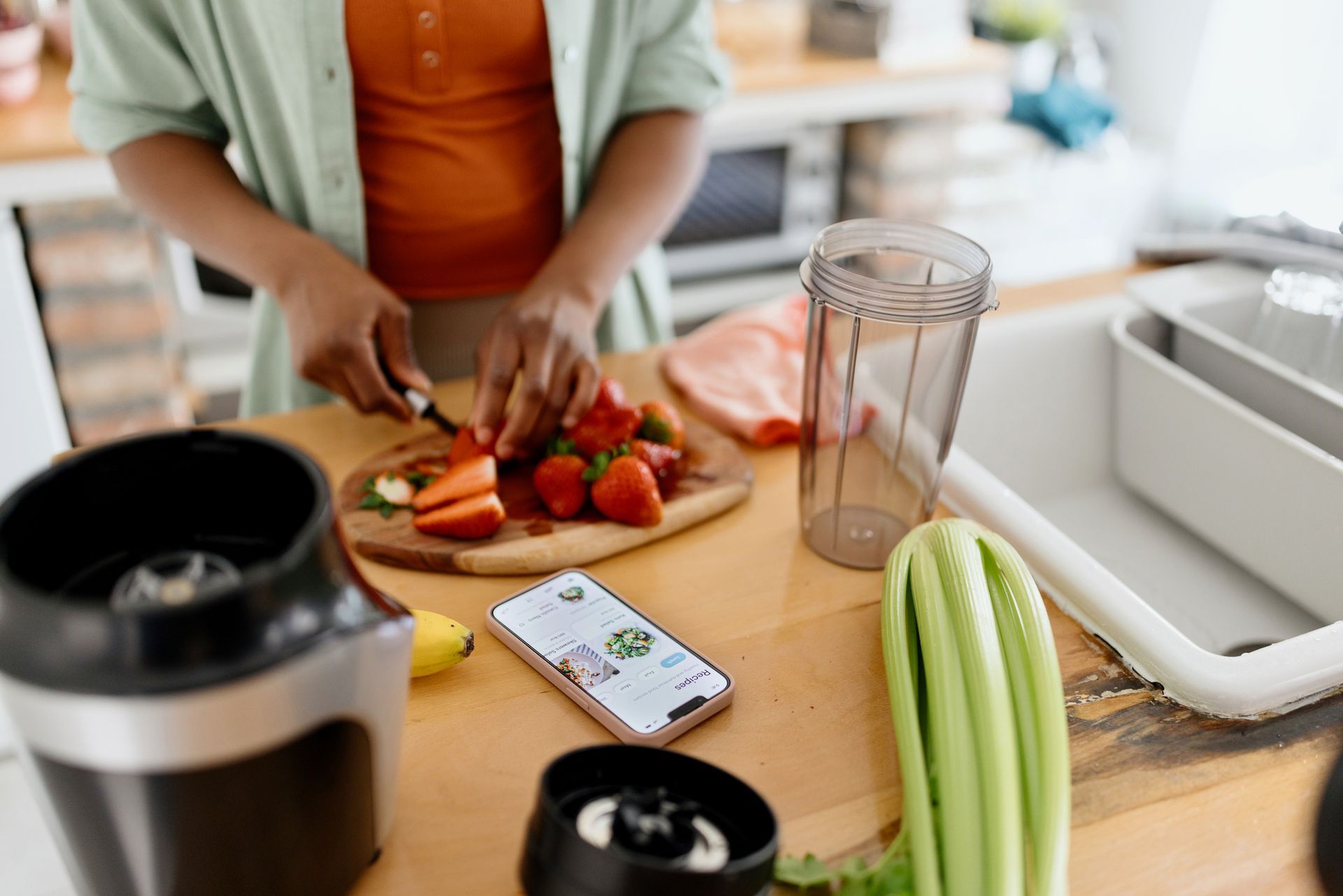 A woman is cutting strawberries on a cutting board in a kitchen.