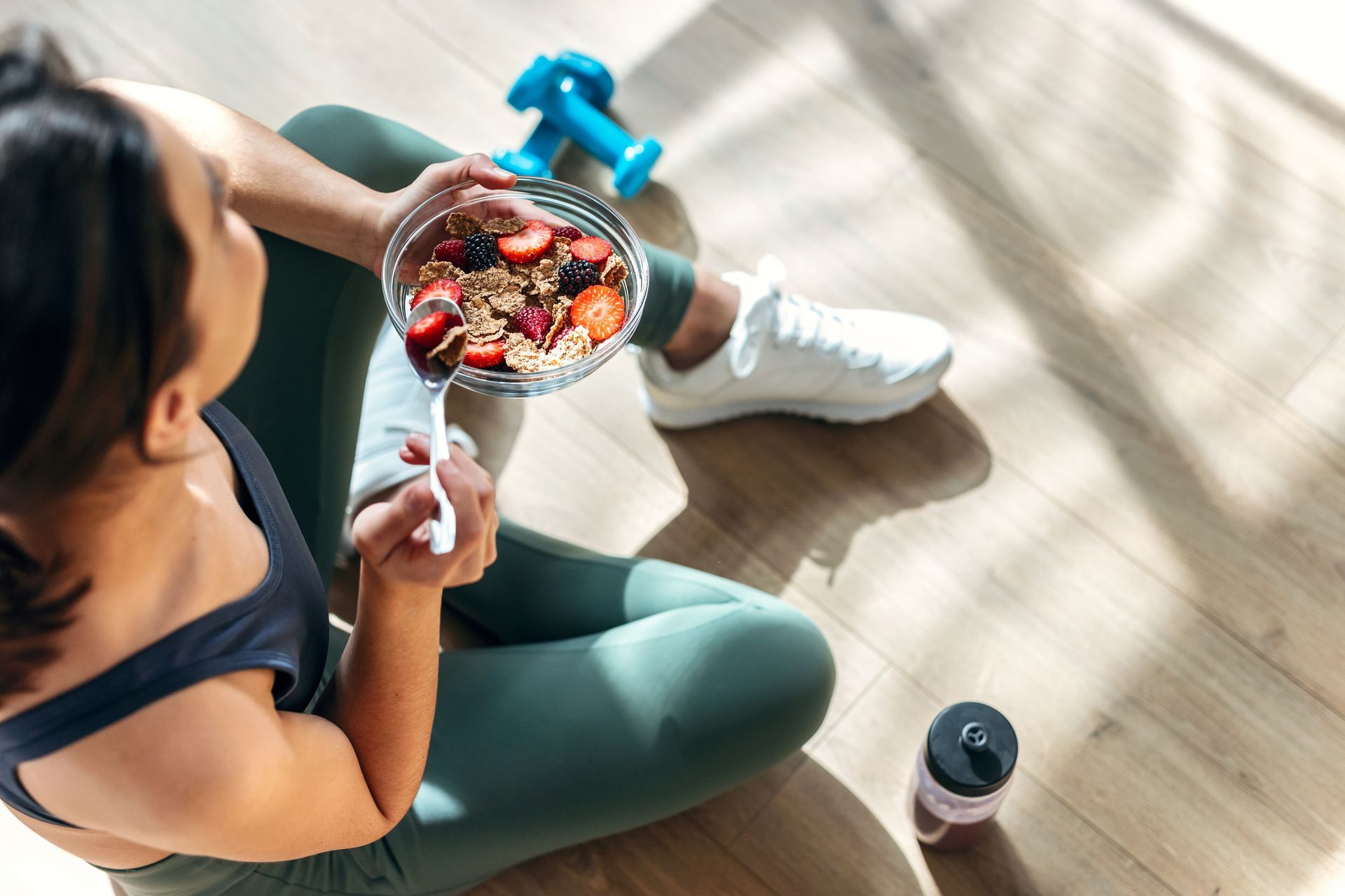 A woman is sitting on the floor eating a bowl of cereal.