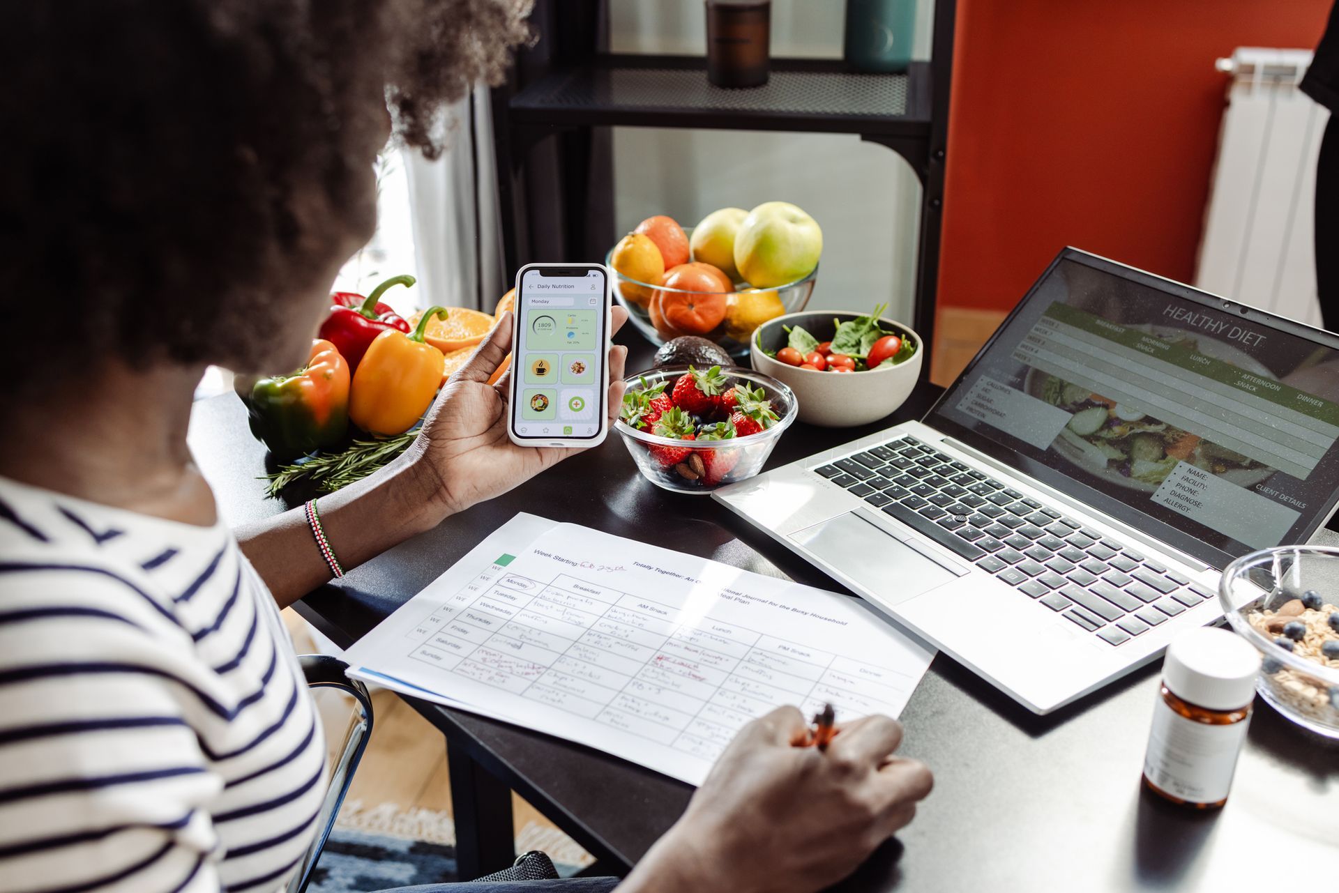 A woman is sitting at a table using a laptop and a cell phone.