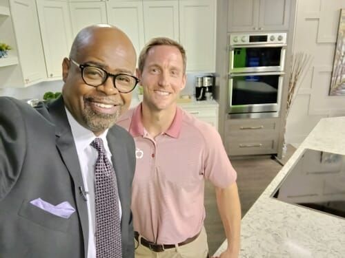 A man in a suit and tie is standing next to another man in a kitchen.