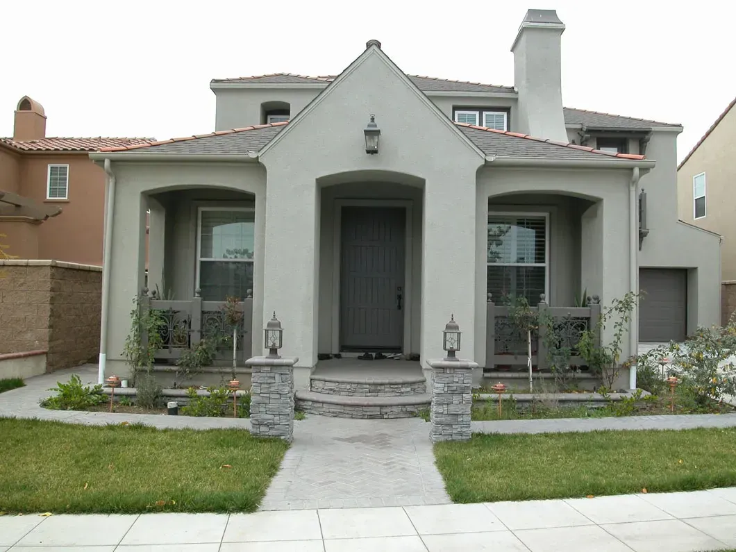 Two-story house with gray stucco exterior, arched front porch, and brick walkway.