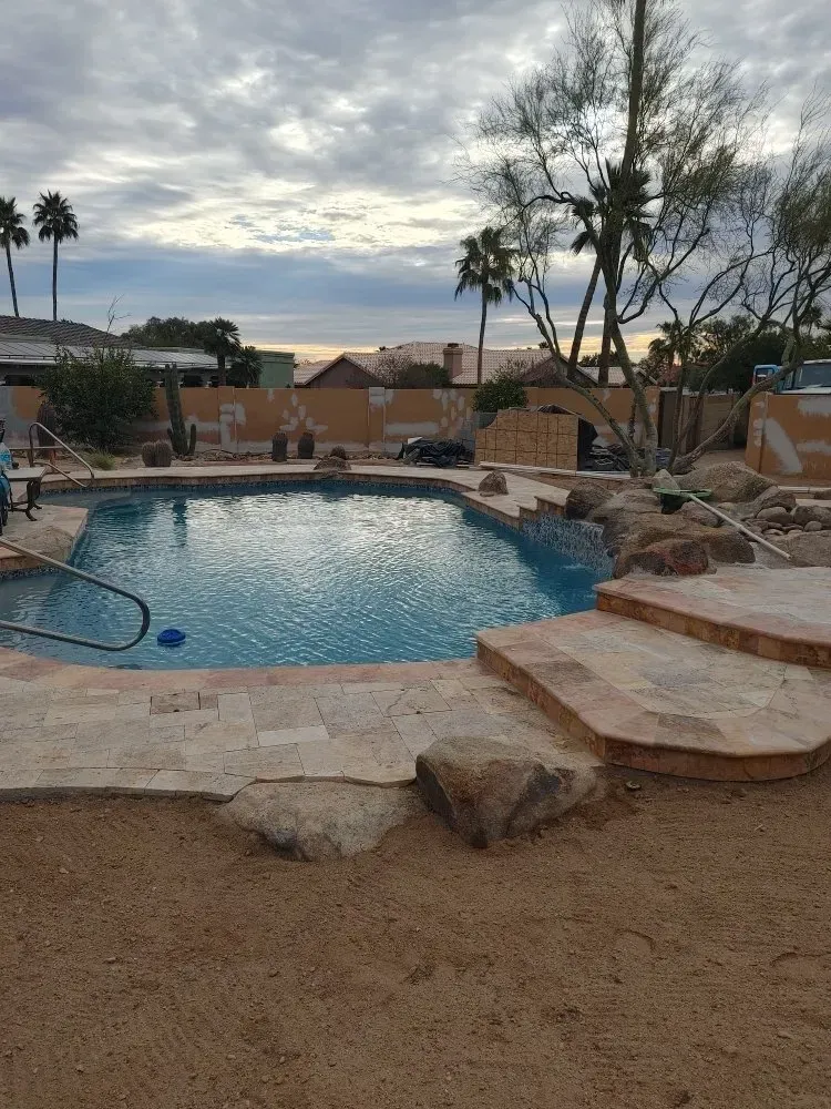 Pool with stone steps, a handrail, and desert landscaping under a cloudy sky.