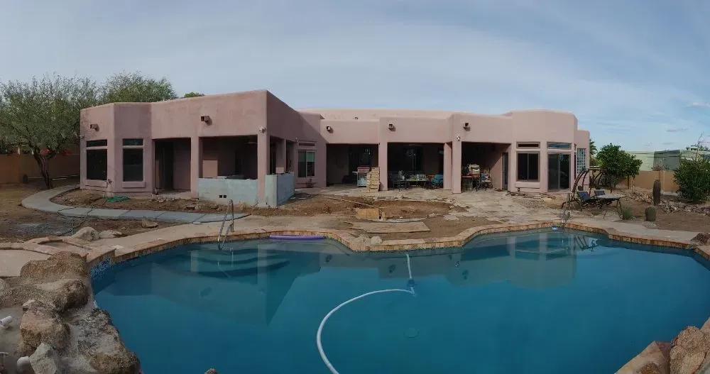 A pink stucco house with a blue pool in front. Landscaping is in progress.