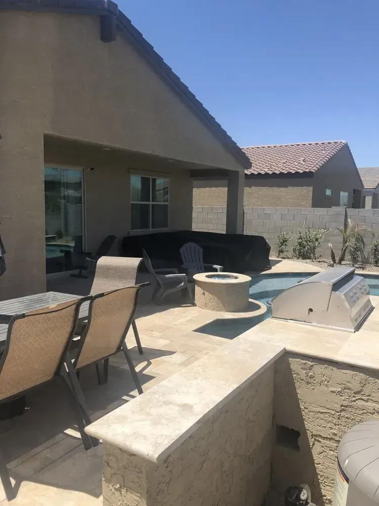Backyard patio with pool, fire pit, grill, and seating under a covered area and chairs around table.