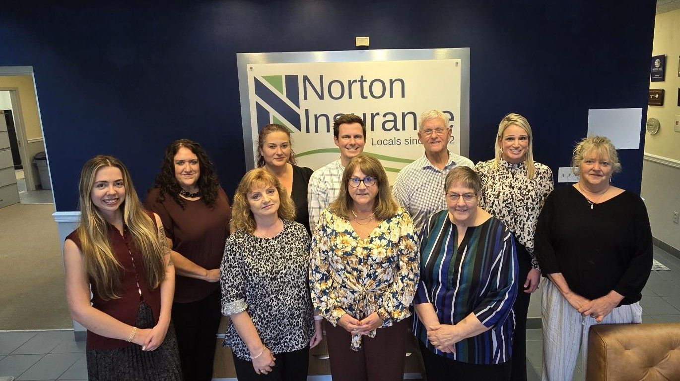 Nine people pose in front of a Norton banner at an indoor event.