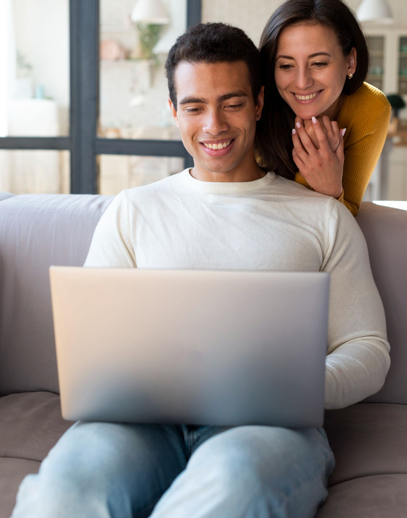 Two people smiling on a couch while looking at a laptop