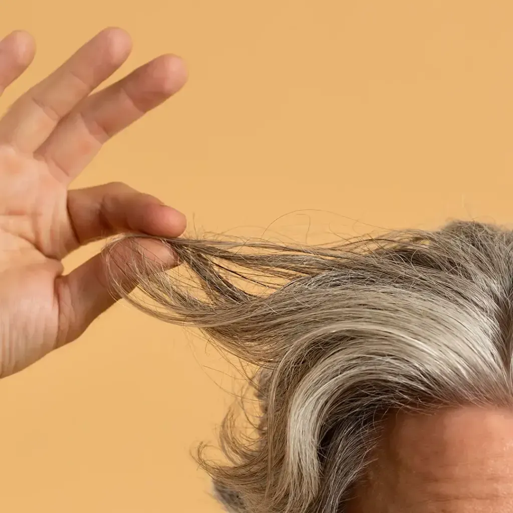 Hand pulling a gray strand of hair against a warm orange background