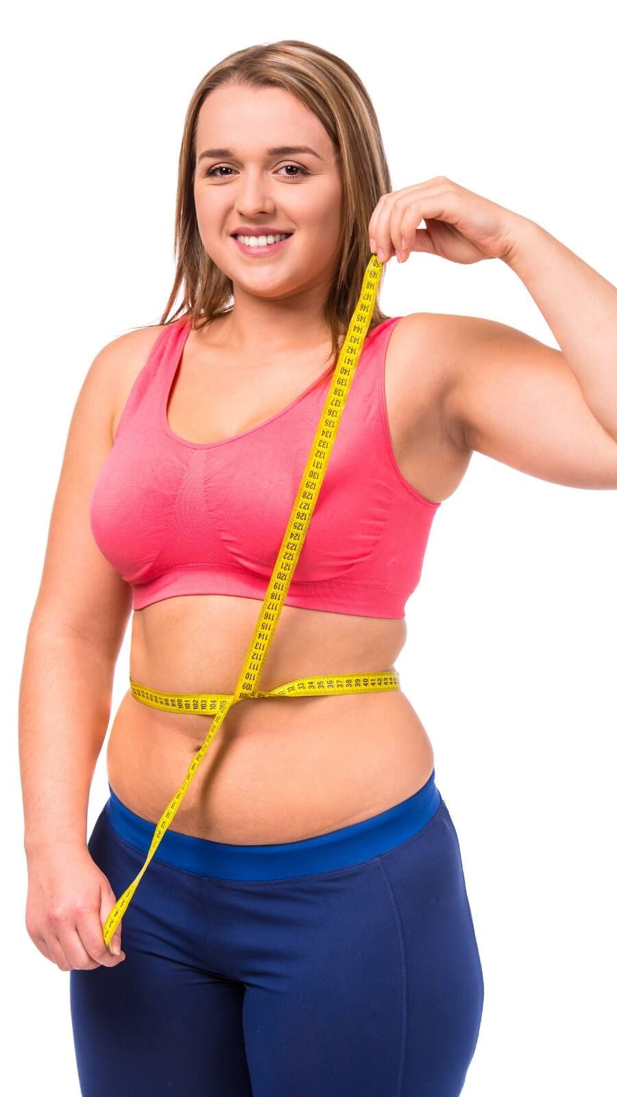 Woman in pink sports bra and blue leggings measuring her waist with a yellow tape measure.