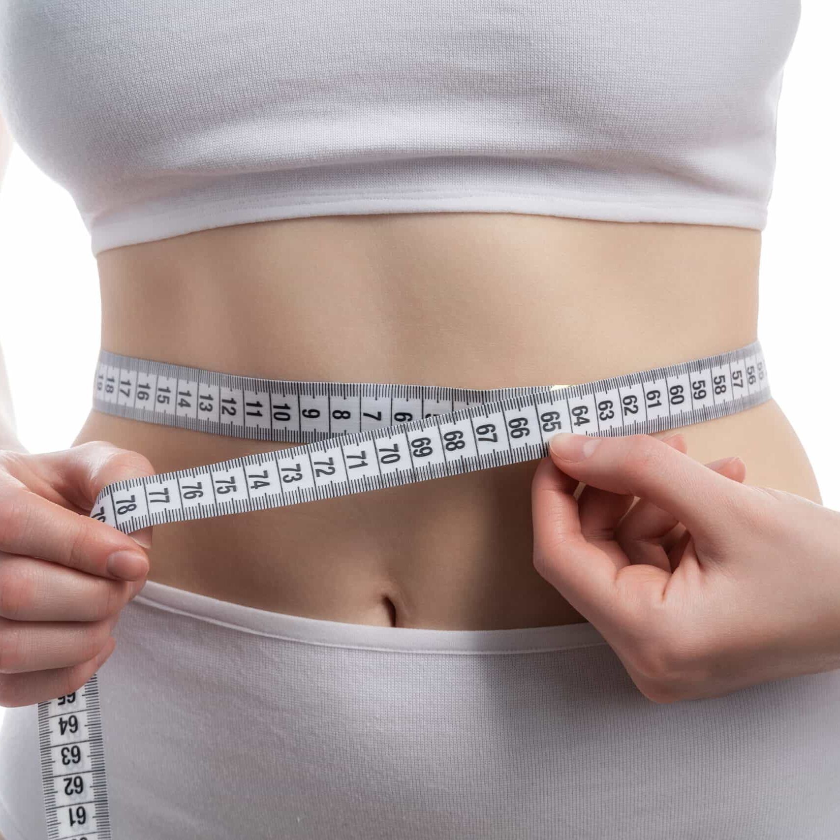Person measuring waist with a tape measure on a white background.