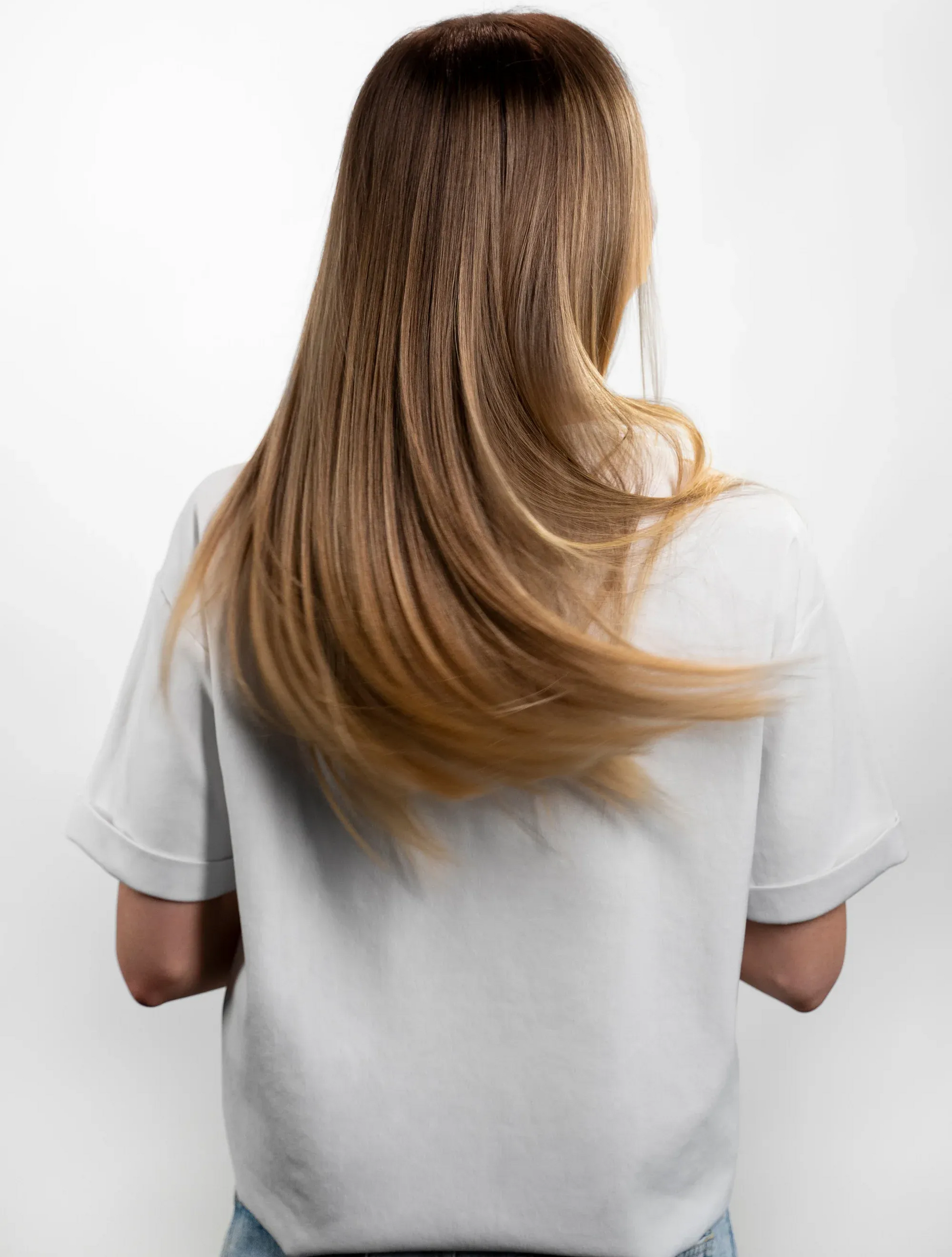 Back view of a person with long brown hair wearing a white shirt against a white background
