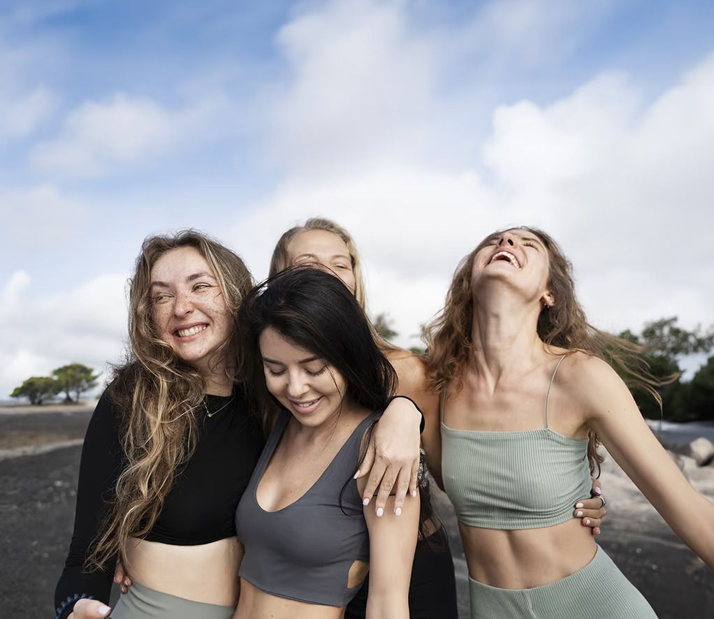 Four friends smiling and dancing outdoors under a cloudy blue sky