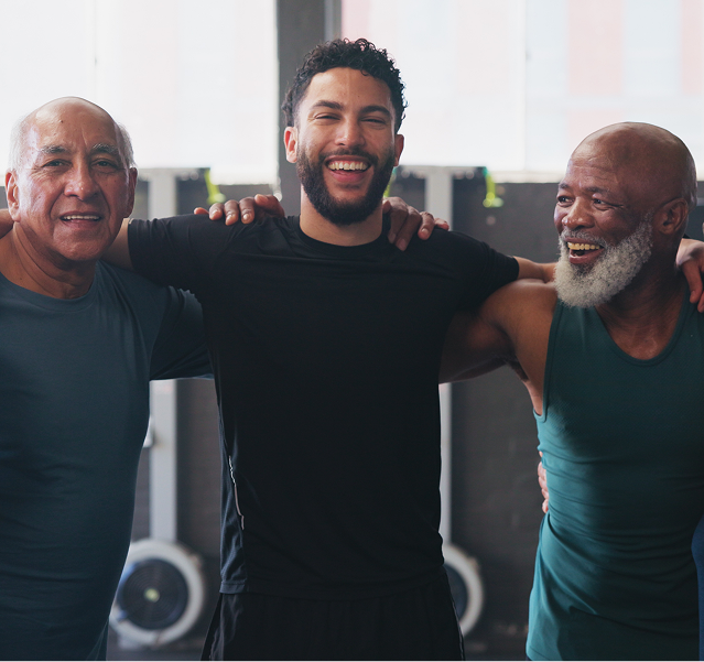 Three men smiling and embracing in a gym, wearing dark workout clothes.