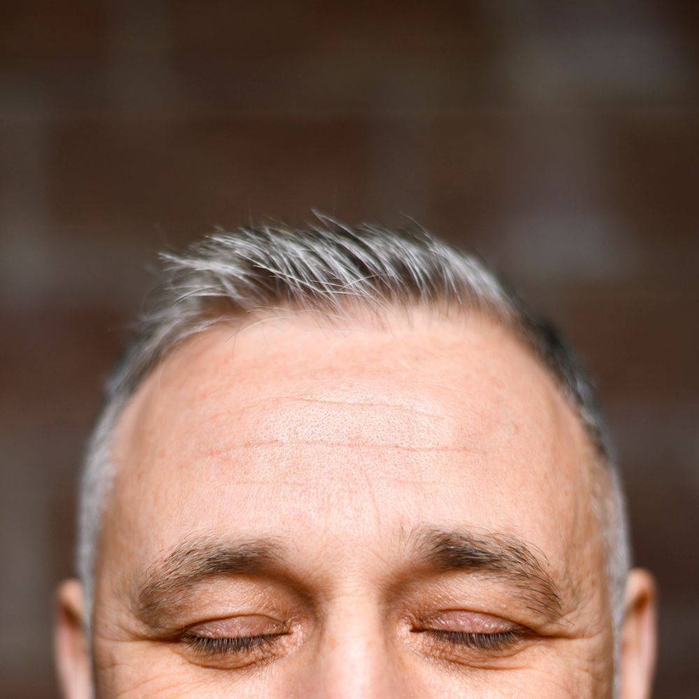 Close-up of a man's forehead and closed eyes against a blurred background