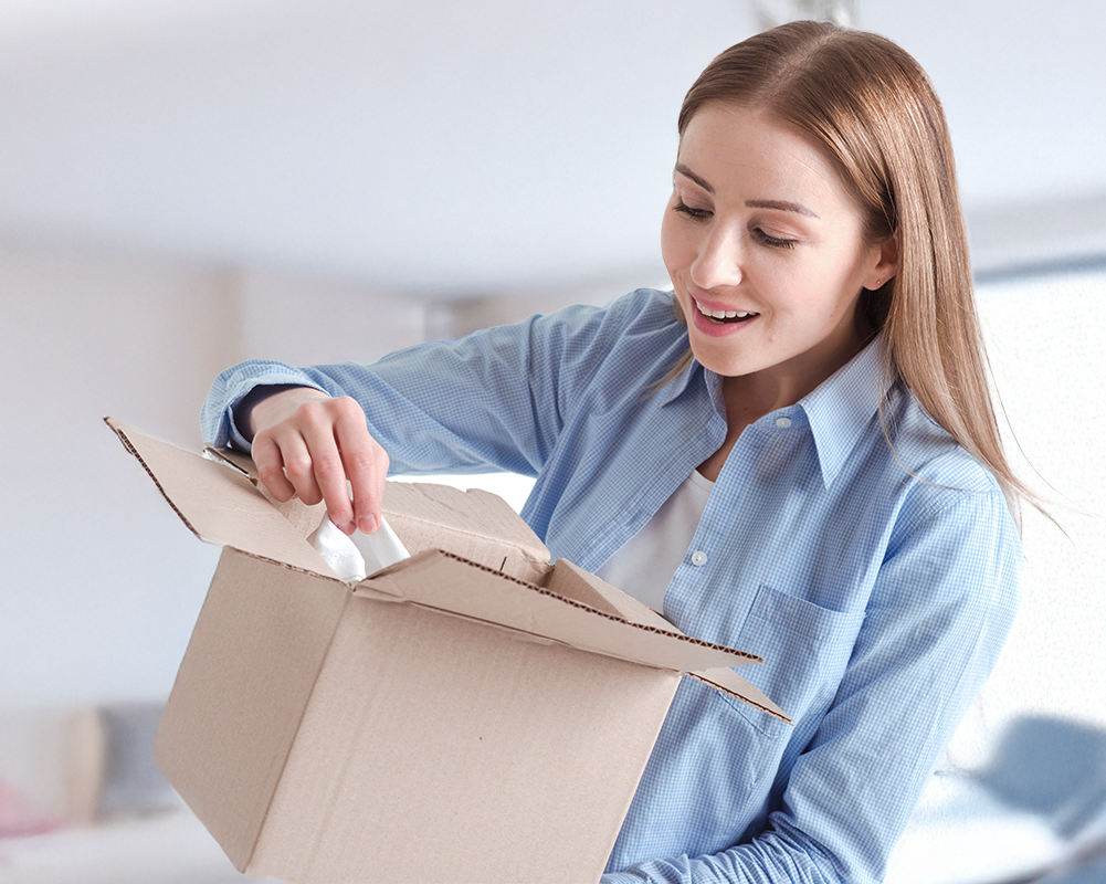 Woman opening a cardboard box and reaching inside in a bright room