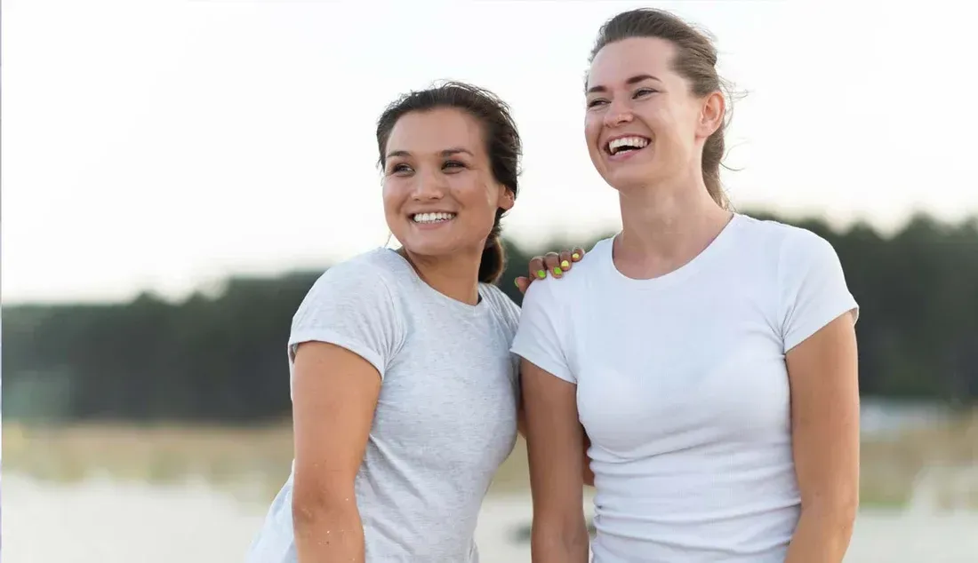 Two smiling people in white T-shirts standing outdoors with a blurred background