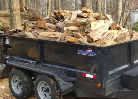 Black trailer filled with firewood, parked outdoors.