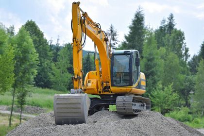 Excavatrice jaune sur un tas de gravier avec un fond de forêt.
