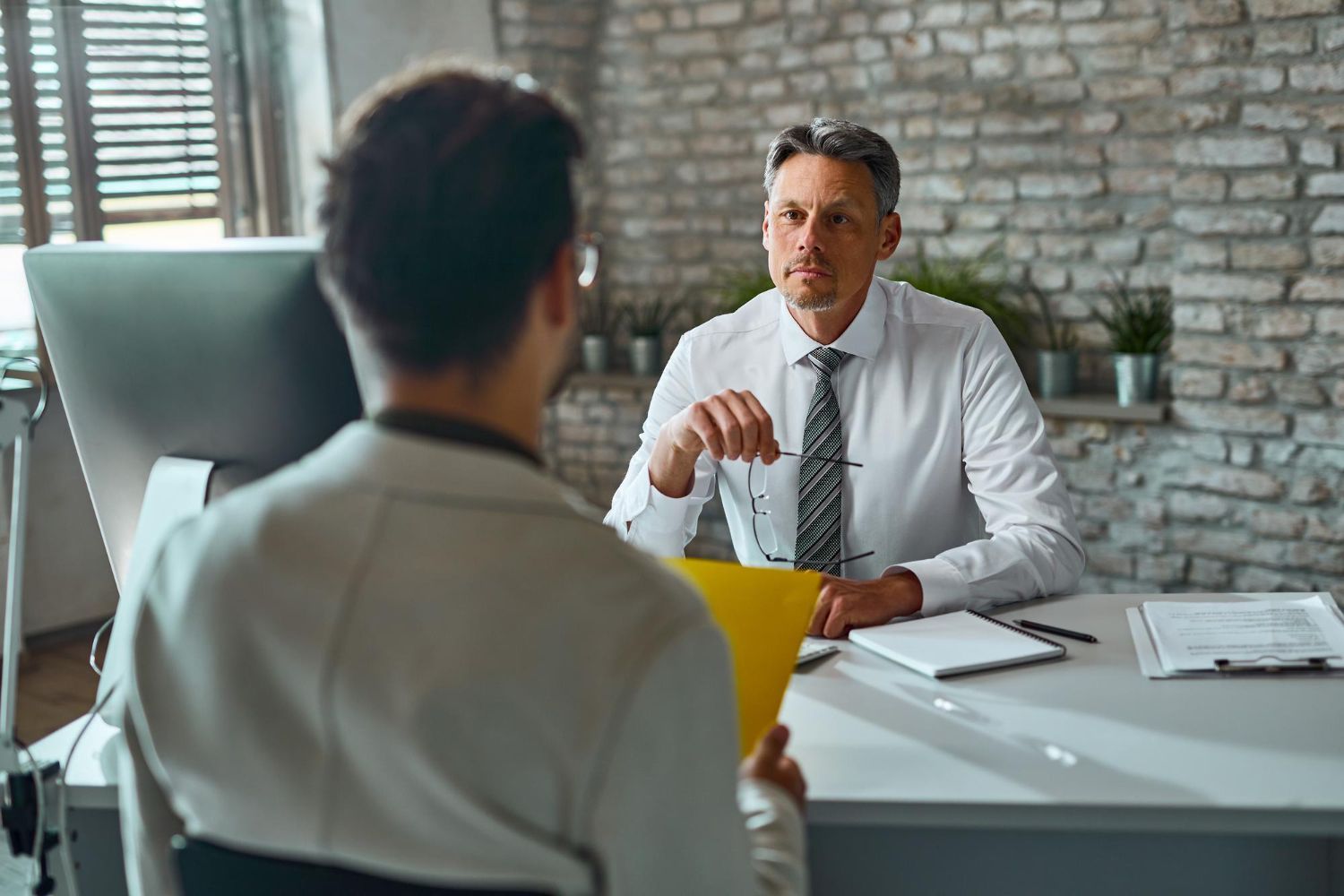Man in white shirt interviewing another at a desk in an office.