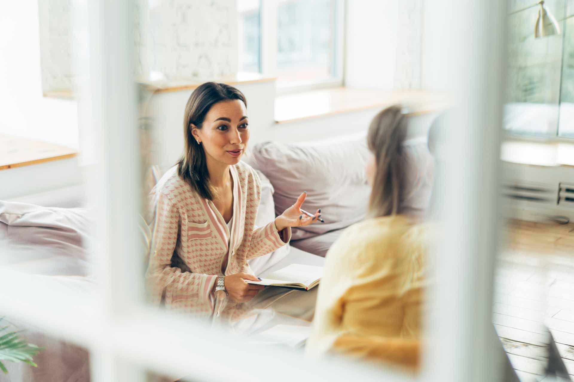 A woman is sitting on a couch talking to another woman.