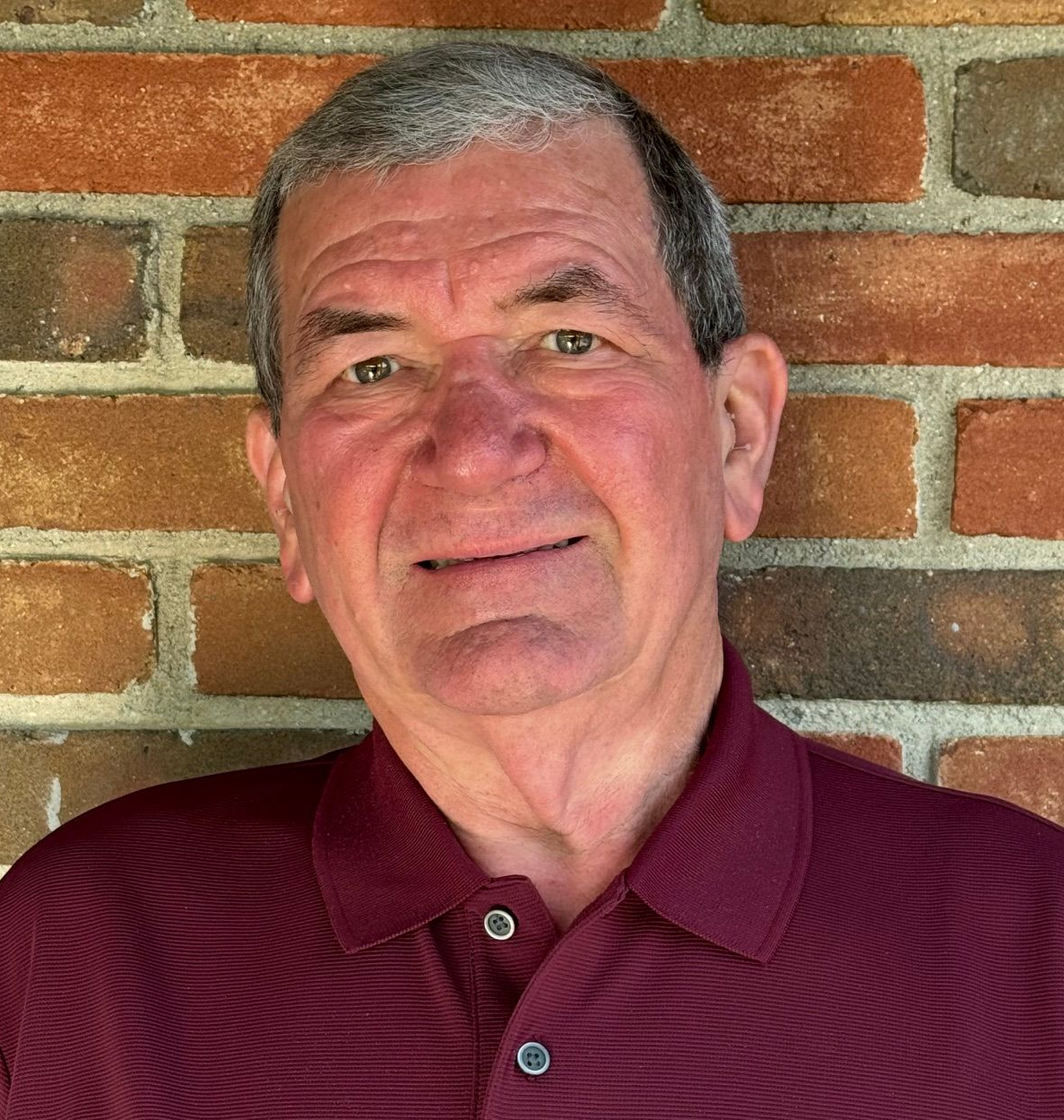 Man in a maroon polo shirt smiling in front of a brick wall