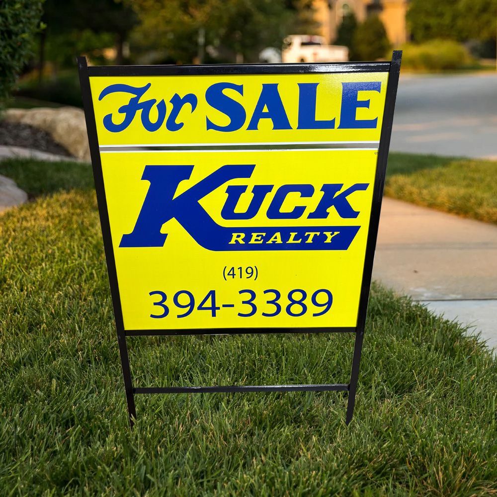 Yellow and blue For Sale sign for Kuck Realty on a lawn, with phone number 394-3389