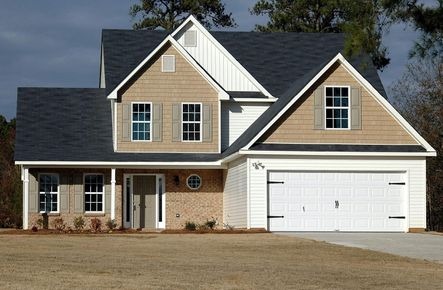 Suburban house with beige siding, dark roof, and white garage door on a gravel driveway