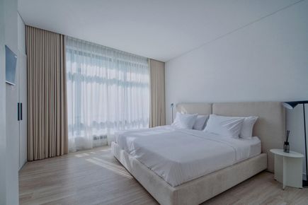 Bright modern bedroom with a large bed, sheer curtains, and soft neutral decor