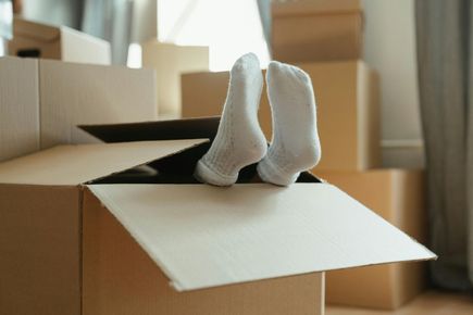 Person’s socked feet sticking out of a cardboard moving box in a room with packed boxes